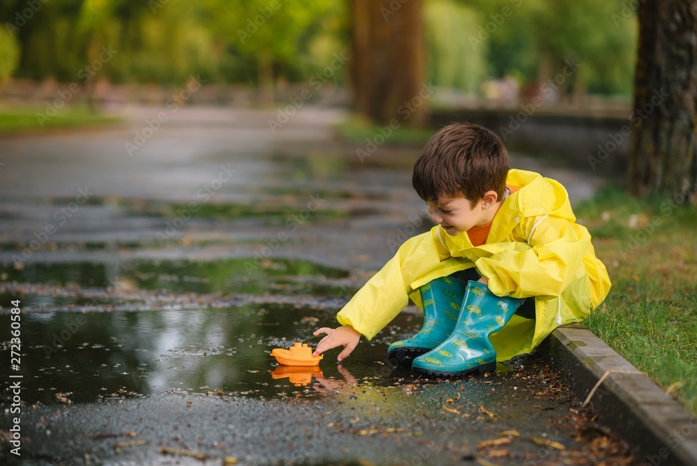 Child playing with toy boat in puddle. Kid play outdoor by ...