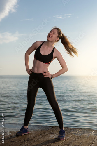 happy girl training near the sea or ocean, morning fitness, in backlight, girl laughs, performs exercises, concept