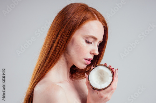 young ginger redhead woman with ideal skin and perfect redhaired hear holding coco nut in hands in white studio backgroung.