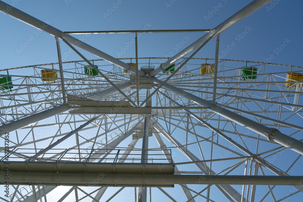 Ferris wheel with yellow and green booths against a blue sky