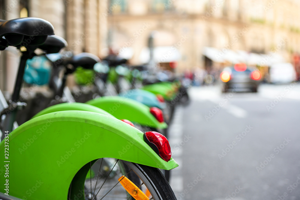 Row of green bikes for public rent stand at parking station on street in Paris ready for use