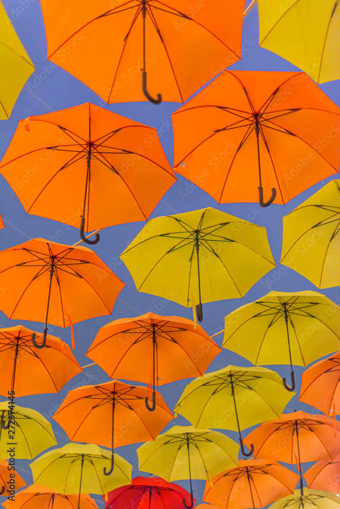 Obraz premium Yellow and orange umbrellas hanging in the air.