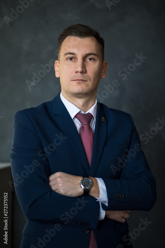 Portrait of young intelligent man lawyer standing with crossed arms in modern office building interior, successful male bank employee dressed in luxury suit posing with copy space area for your text