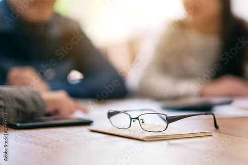 Close up image of black eyeglasses on notebook with blur businessman in office