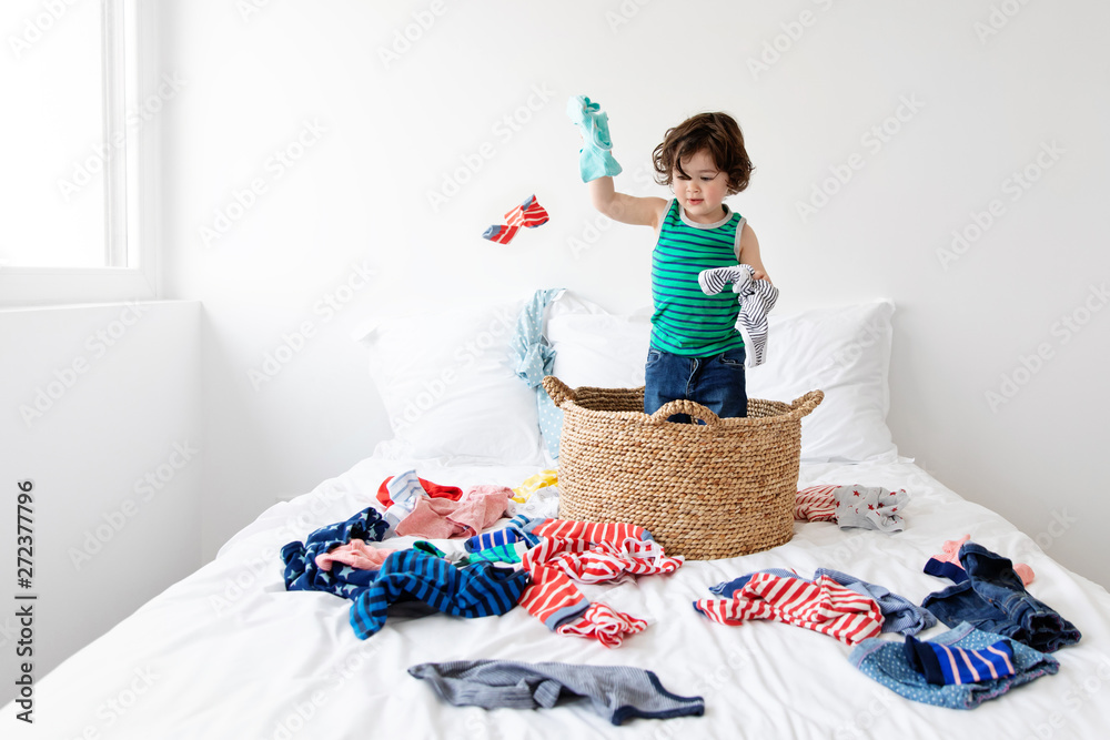 Young child standing in laundry basket throwing clothes Stock Photo