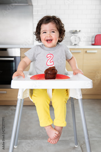 Smiling child in high chair with cake celebrating second birthday photo