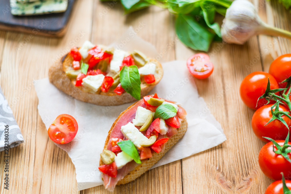 Traditional Italian bruschetta with blue cheese, feta, tomatoes, basil leaves, jamon on a wooden background.