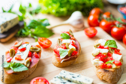 Traditional Italian bruschetta with blue cheese, feta, tomatoes, basil leaves, jamon on a wooden background.