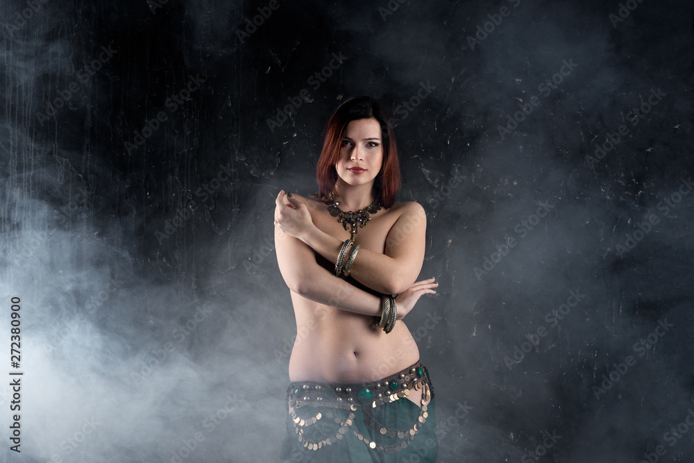 Fototapeta premium Sexy women performs belly dance in ethnic dress on dark smoky background, abstract art photography