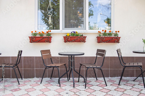 Glass and metal tables and chairs on a summer terrace cafe by the window with pots of flowers © svitlini