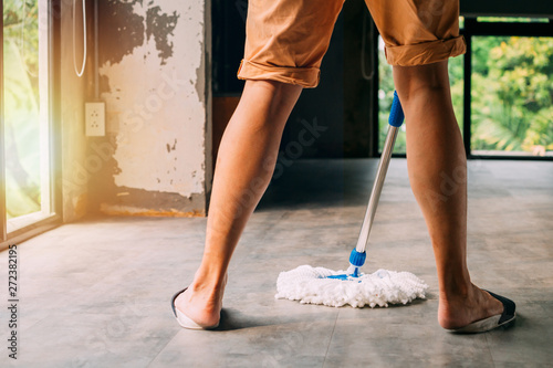 Low section of human legs and feet wearing slippers using mopping tool to clean up inside the living room at home - cleanliness and housekeeping concept