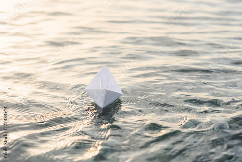 Alone paper boat floats on the water at sunset.