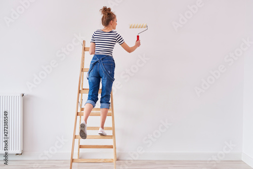 Fototapeta Naklejka Na Ścianę i Meble -  Rear view of woman with paint roller painting wall