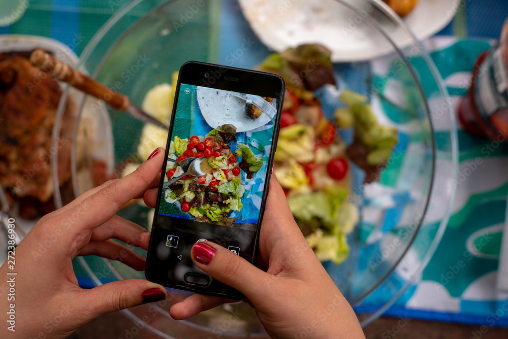 a woman's hand is holding a phone and taking pictures of food on the table, on screen of phone you can see the dishes a woman's hand is holding a phone and taking pictures of food on the table, on screen of phone you can see the dishes