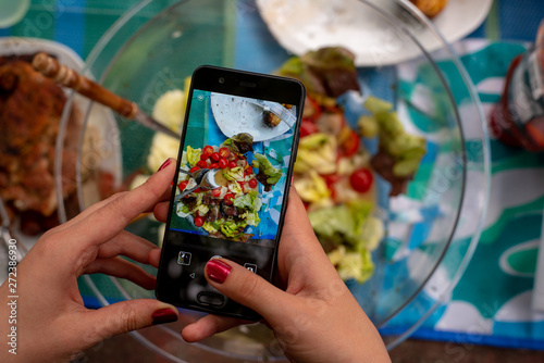 a woman's hand is holding a phone and taking pictures of food on the table, on screen of phone you can see the dishes