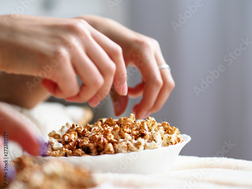Female hands taking popcorn grains out from bowl while watching tv