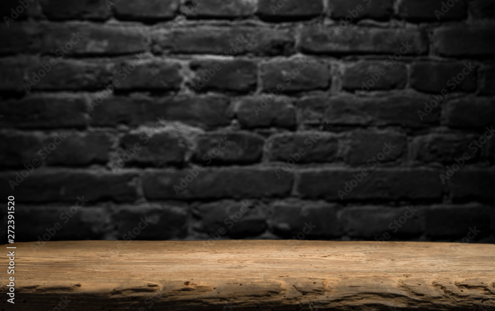 Obraz premium Old wood table with blurred concrete block wall in dark room background.