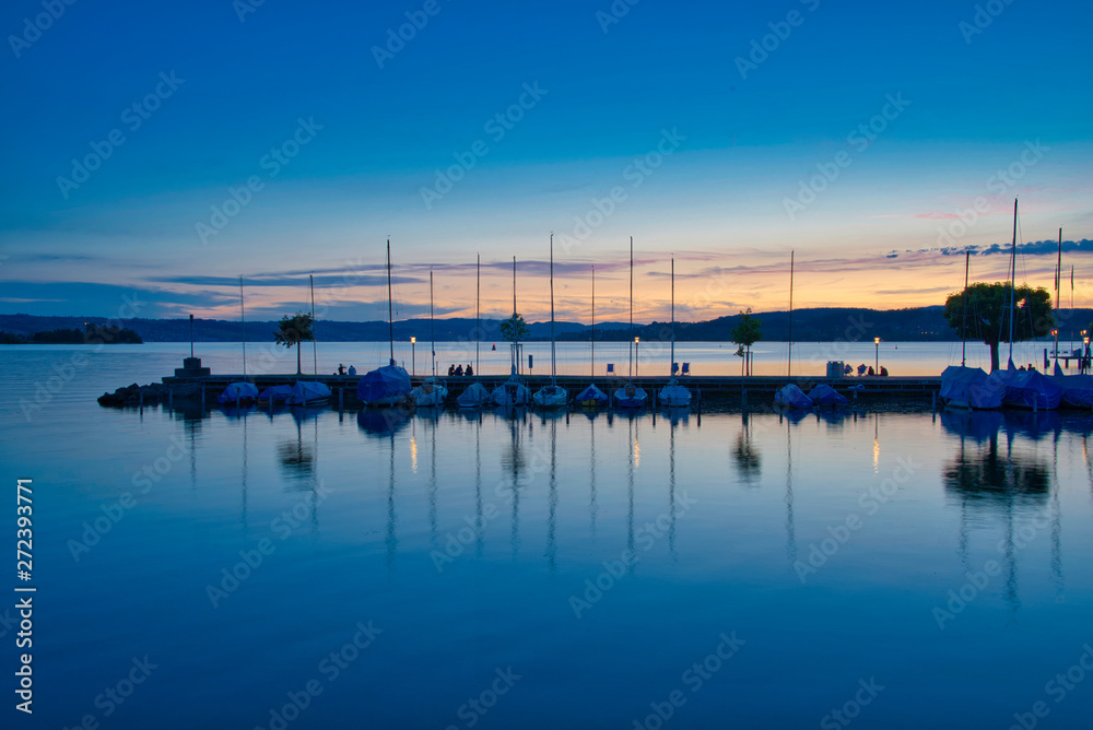 Sonnenuntergang am Seeufer mit Booten und Menschen