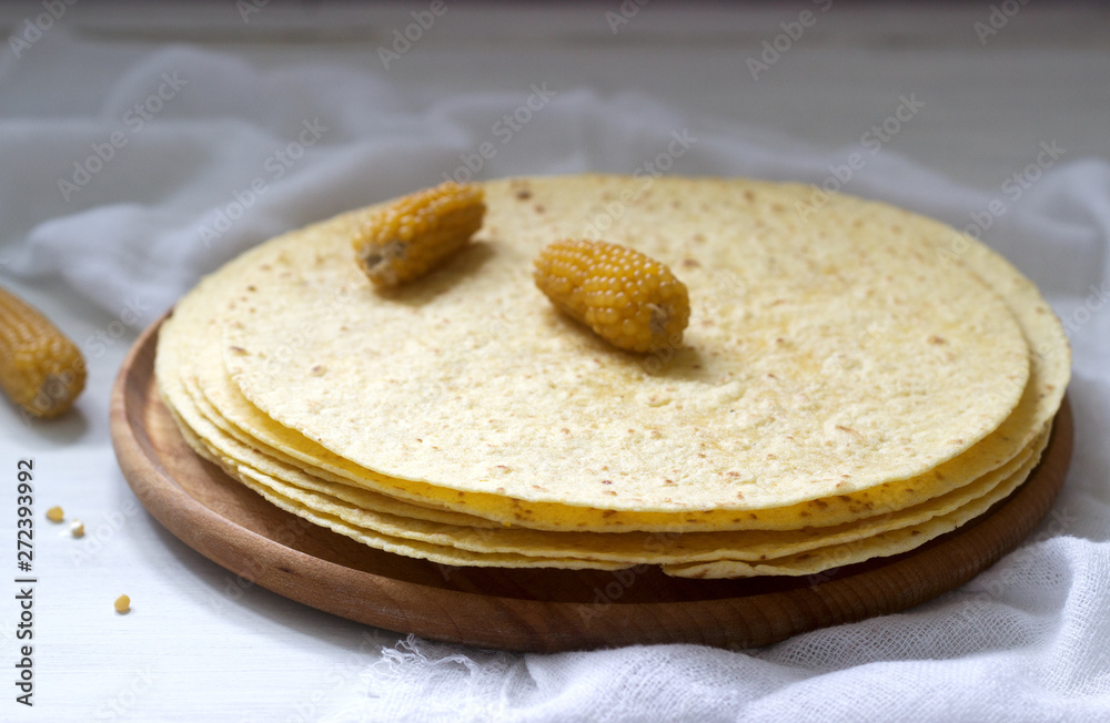 A stack of round corn tortillas on a wooden board and corncobs. A stack of round corn tortillas on a wooden board and corncobs.