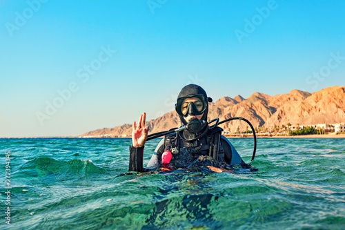 Woman diver floated on the surface of the sea and shows a hand sign that all is well.