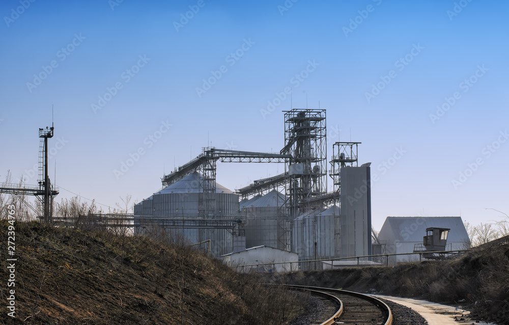 Obraz premium View of modern sugar factory with industrial silos (large metal tanks for sugar, grain or silage storage), buildings, towers and other metal structures and equipment, blue sky background