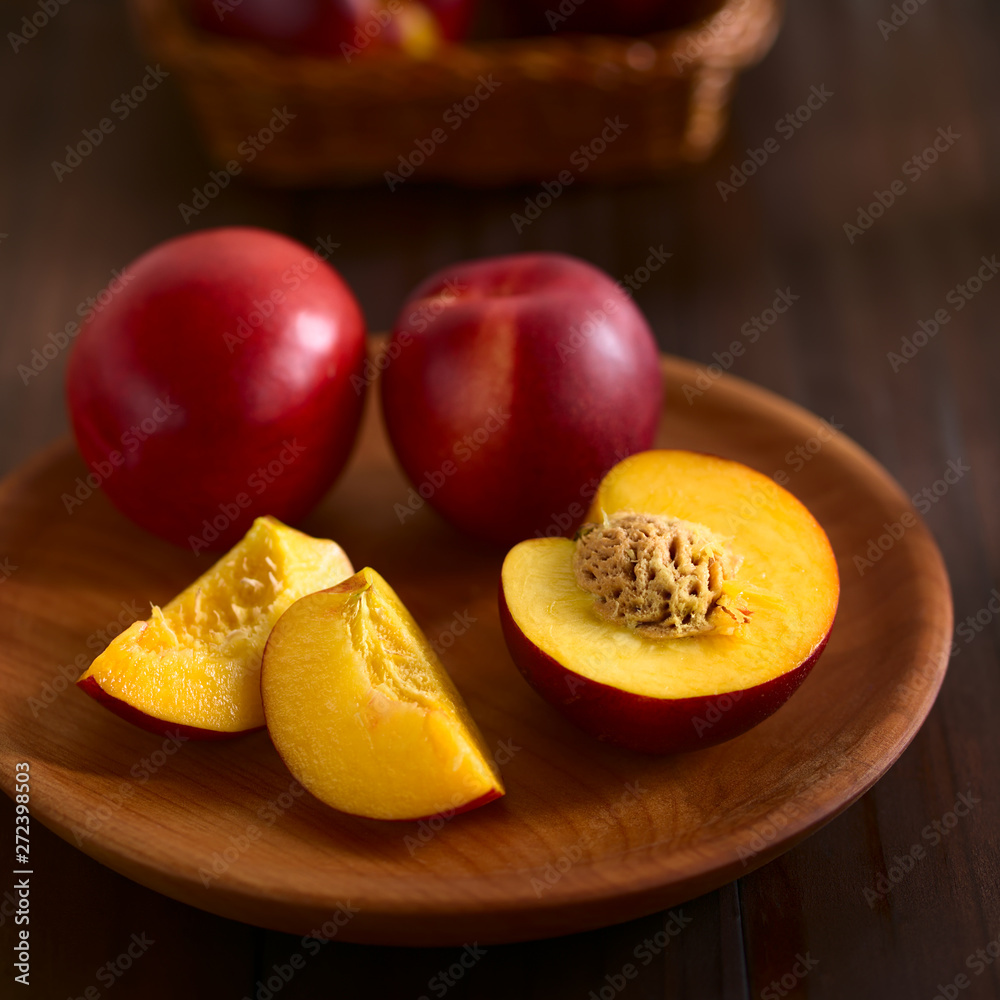 Fresh ripe nectarine fruits cut and whole on wooden plate, photographed on dark wood with natural light (Selective Focus, Focus on the front of the seed in the nectarine half) Fresh ripe nectarine fruits cut and whole on wooden plate, photographed on dark wood with natural light (Selective Focus, Focus on the front of the seed in the nectarine half)