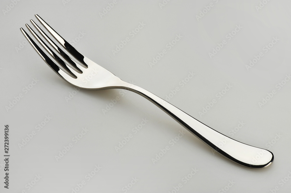 One dining fork resting on a gray surface One dining fork resting on a gray surface