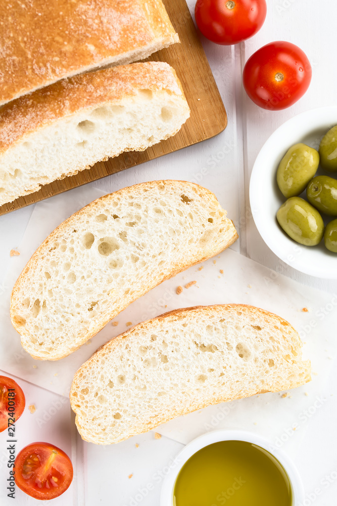 Frisches italienisches Ciabatta Brot in Scheiben geschnitten, Kirschtomaten, Oliven und Olivenöl an der Seite (Selektiver Fokus, Fokus auf die Brotscheiben) Frisches italienisches Ciabatta Brot in Scheiben geschnitten, Kirschtomaten, Oliven und Olivenöl an der Seite (Selektiver Fokus, Fokus auf die Brotscheiben)