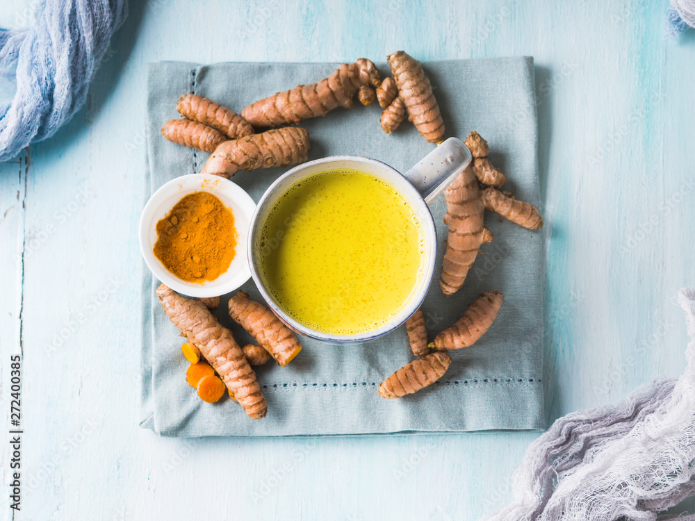 Golden turmeric coconut milk drink in mug on pastel background. Healthy