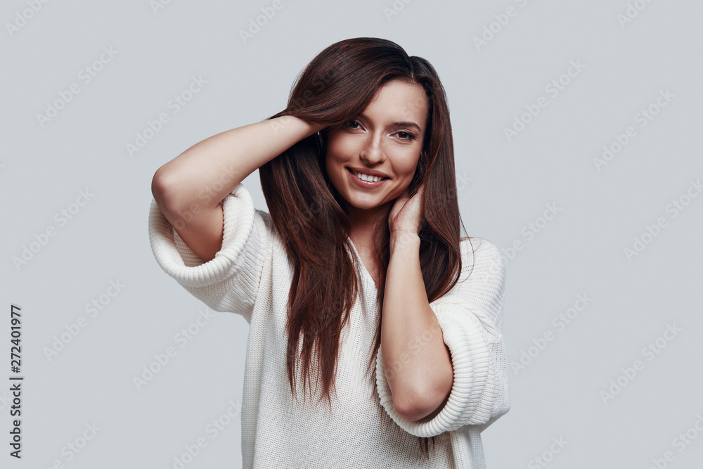 Cute beauty. Attractive young woman looking at camera and smiling while standing against grey background Cute beauty. Attractive young woman looking at camera and smiling while standing against grey background
