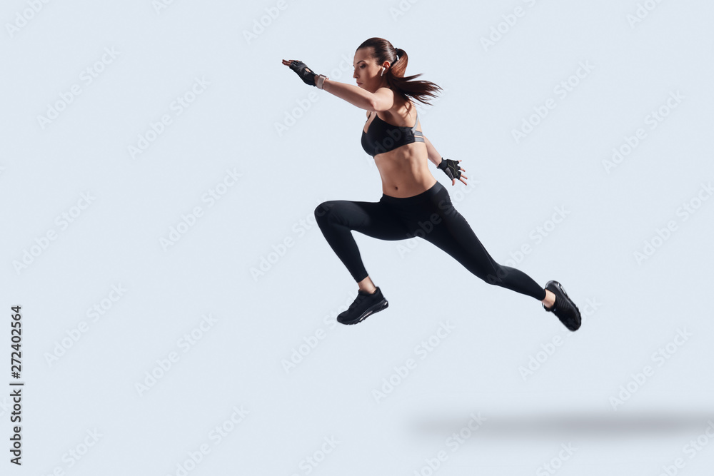 Motivated to shape her body. Full length of attractive young woman in sports clothing exercising while hovering against grey background