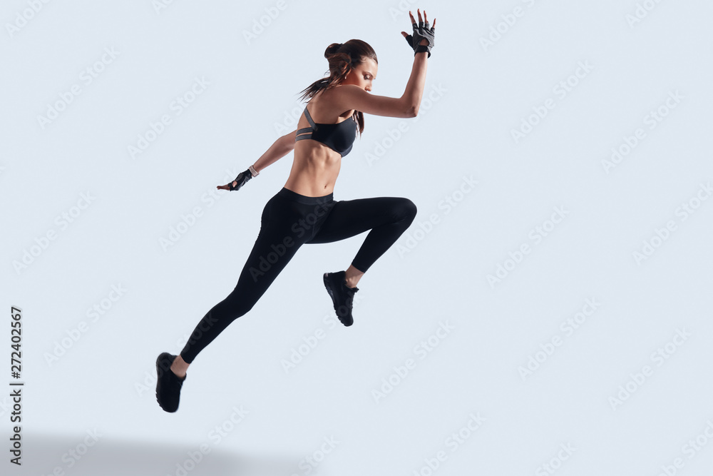 Real freedom. Full length of attractive young woman in sports clothing exercising while hovering against grey background