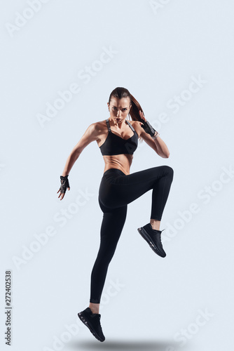 Keep moving! Full length of attractive young woman in sports clothing looking at camera while hovering against grey background