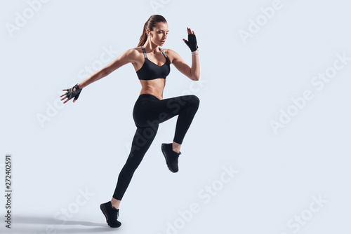 Determined to win. Full length of attractive young woman in sports clothing jumping while hovering against grey background