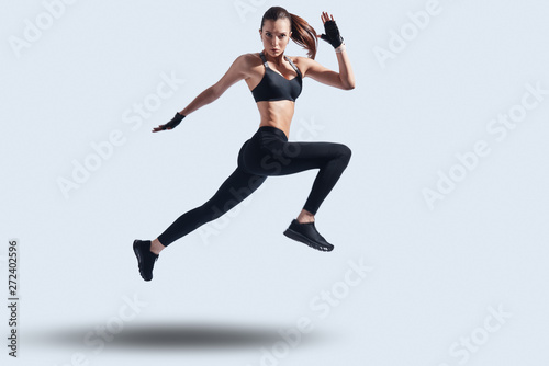 Act now! Full length of attractive young woman in sports clothing looking at camera while hovering against grey background
