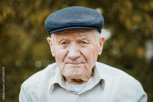 Very old caucasian man portrait. Grandfather in hat. Portrait: aged, elderly, loneliness, senior with lot of wrinkles on face. Close-up of a pensive old man sitting alone outdoors. photo