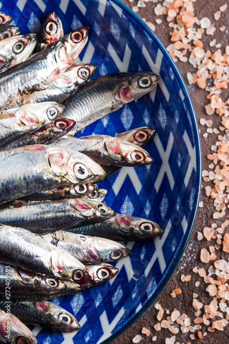 Blue fish. Fresh anchovies in a dish with pink salt on dark brown background. Healthy protein meal. Local seafood, Italy