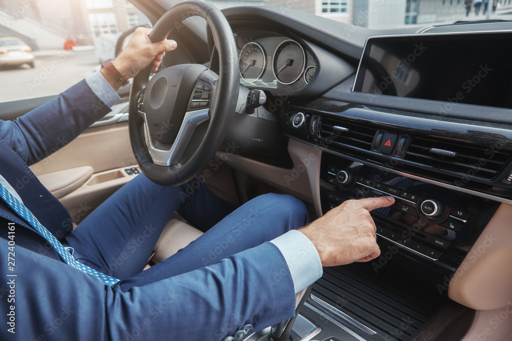 Driving with music. Cropped image of businessman in formal wear pushing buttons of music player while driving to a business meeting