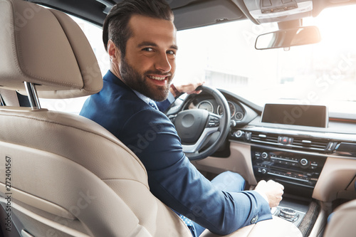 Active and successful. Happy bearded businessman in formal wear looking at camera and smiling while driving his new car.
