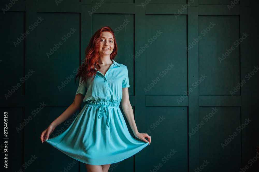 Obraz premium Red-haired girl in blue dress shows hand. on a dark green background. copy space