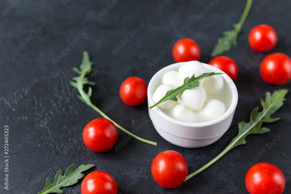 small balls of mozzarella in a bowl with arugula , cherry tomatoes on a black background small balls of mozzarella in a bowl with arugula , cherry tomatoes on a black background