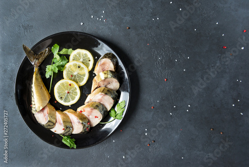 smoked mackerel cut into pieces on a plate on a black background, top view