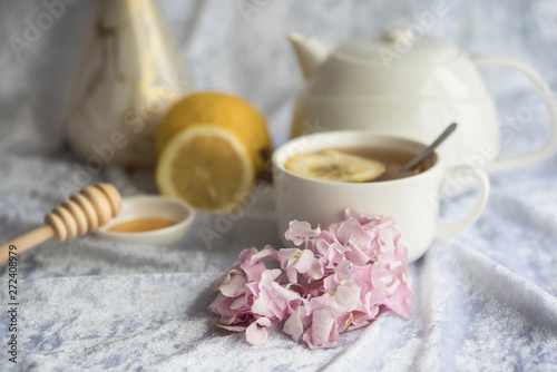 Cup of tea and teapot with lemons and honey on a white background, pink hortensia and a cup of tea, close up