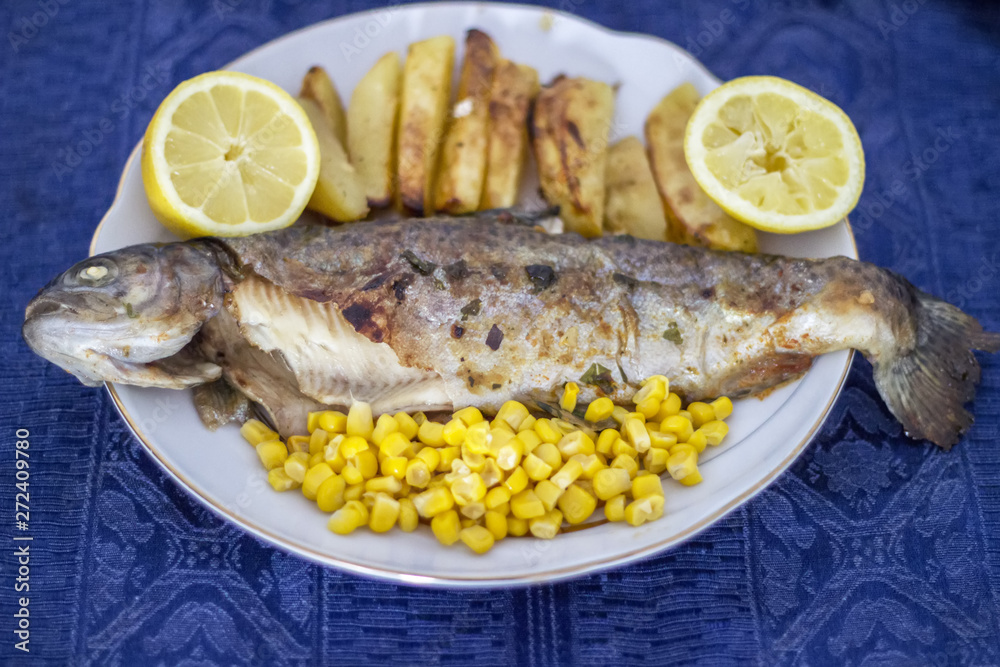 Fish in a plate with potato, lemon and corn. Salmonidae in a plate