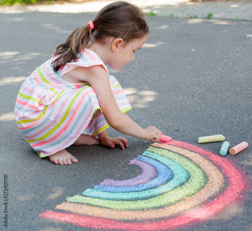 the child girl draws a rainbow with colored chalk on the asphalt. Child drawings paintings concept. Education and arts, be creative when back to school 