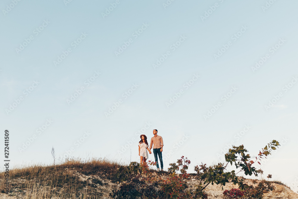 Obraz premium Outdoor shot of young couple in love walking on pathway through grass field. Man and woman walking along tall grass field. 