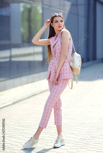 high fashion outdoor Portrait of a young woman. Pantsuit, pink color, long hair, sunglasses