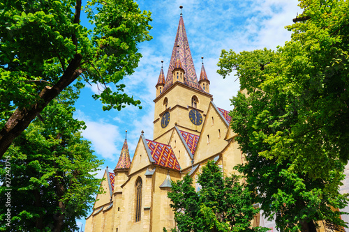 Lutheran Cathedral of Saint Mary (Catedrala Evanghelica C.A. Sfanta Maria) in Sibiu, Romania, view towards the lookout tower, framed by green trees, in bright daylight. Popular touristic spot. photo