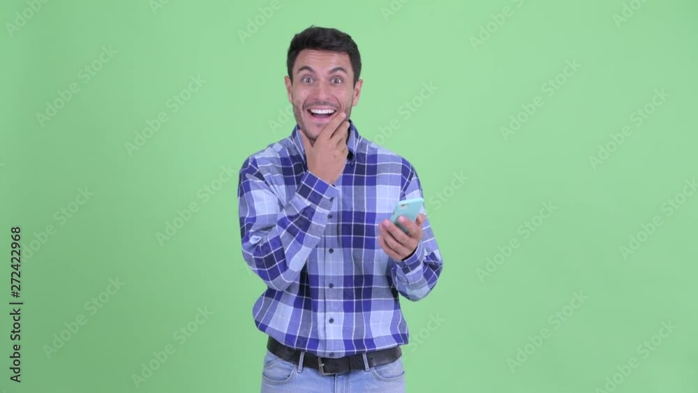 Happy young Hispanic man using phone and looking surprised Happy young Hispanic man using phone and looking surprised