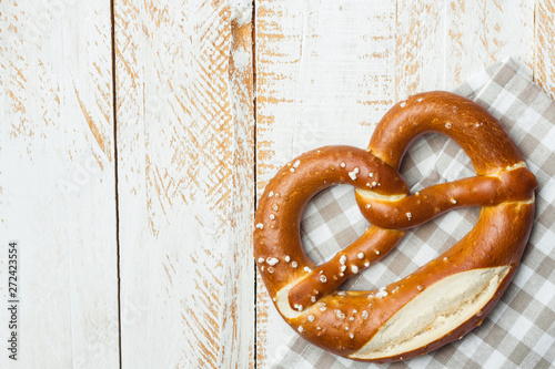 Traditional German savory lye pretzel with salt on checkered cotton kitchen towel on white plank wood table. Poster banner for bakery coffee shop menu. Oktoberfest card. Copy space